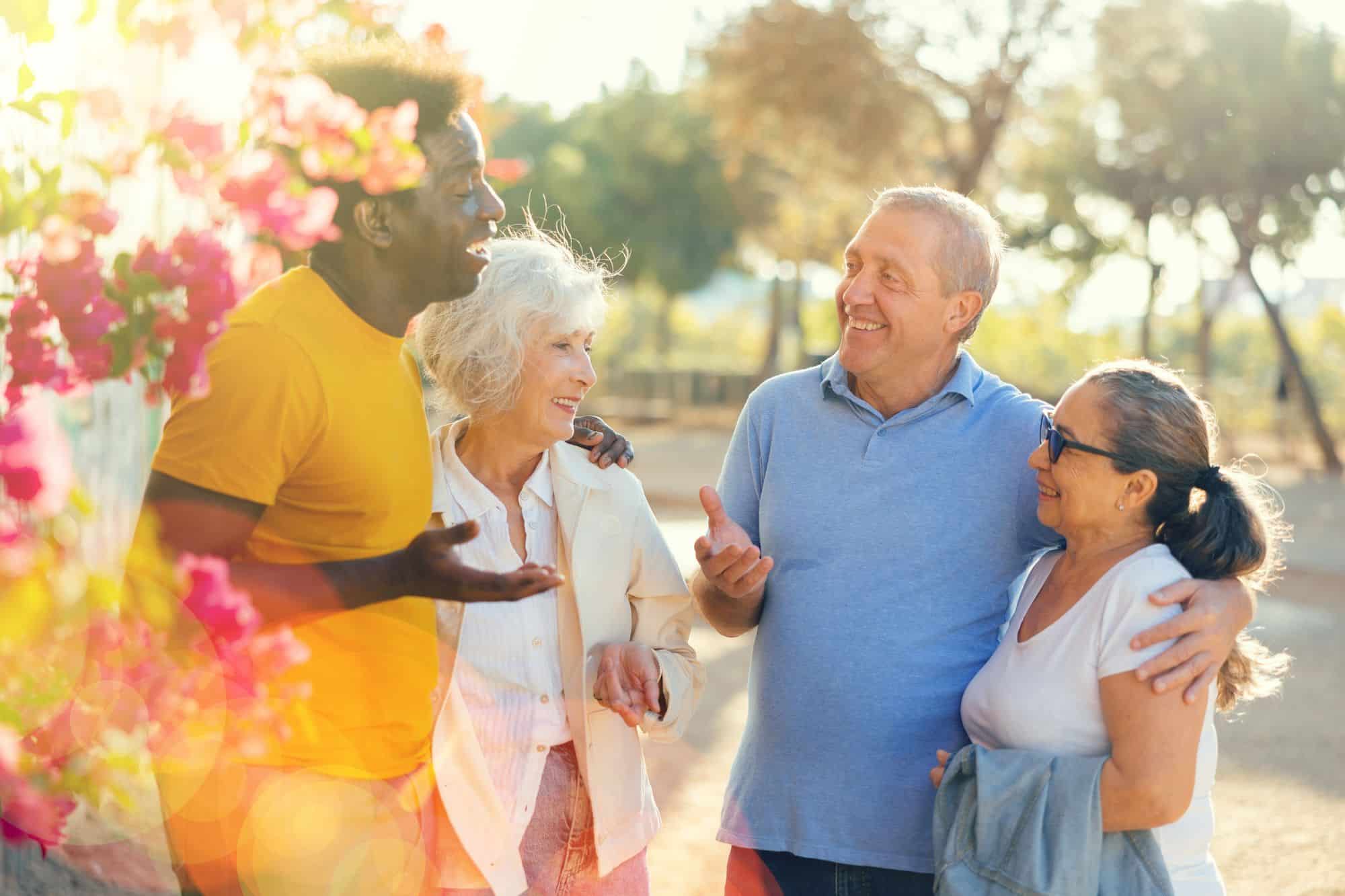 Four older adults smiling and chatting outdoors near pink flowers on a sunny day, enjoying each other’s company in San Tan Valley, AZ